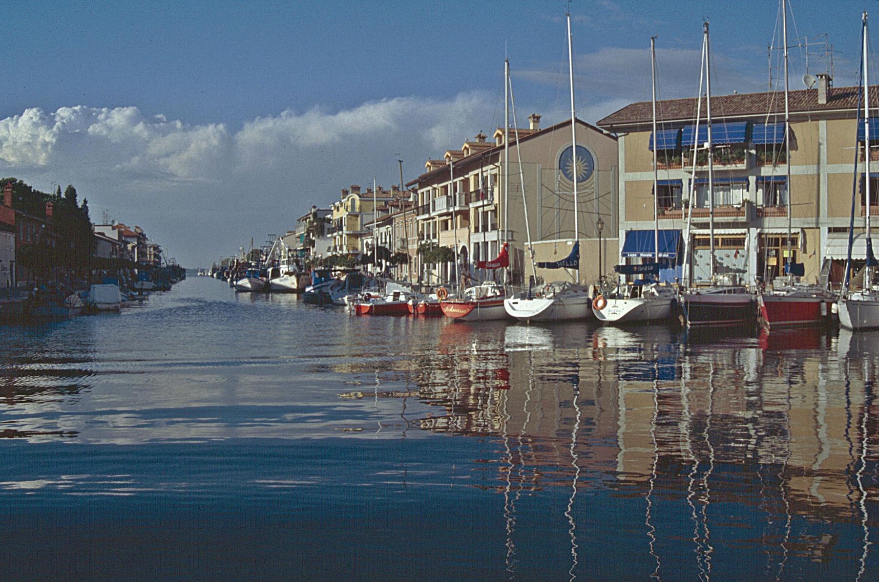 Sailboats and pastel houses reflected in Grado's harbour canal