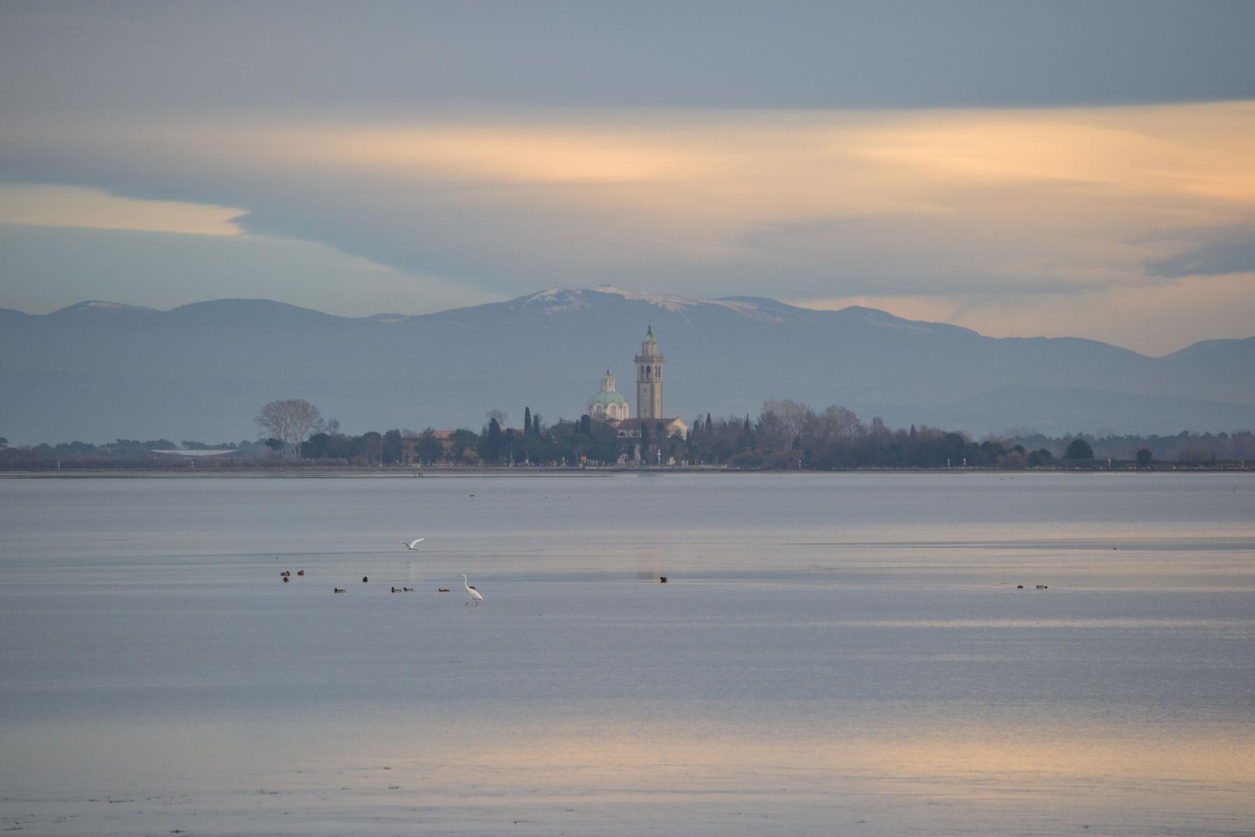 Soft dusk light over the lagoon with Barbana sanctuary and snowy hills