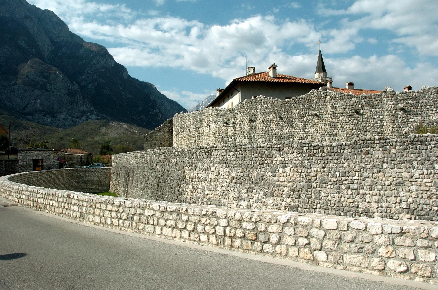 Medieval double curtain walls of Venzone curving beneath a rocky mountain